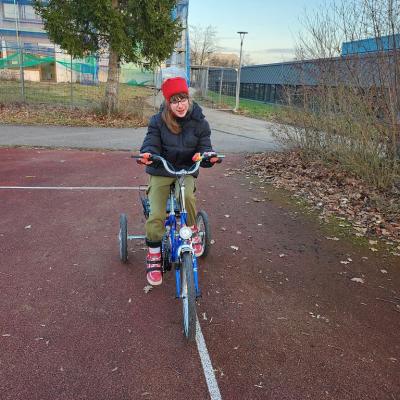 Schülerin sitzt auf einem blauen Fahrrad und fährt genau auf der Linie auf dem roten Sportplatz
