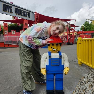 Ein Mädchen steht neben einem großen Legomännchen. Sie lächelt und legt ihren Kopf auf den Kopf des Männchens 