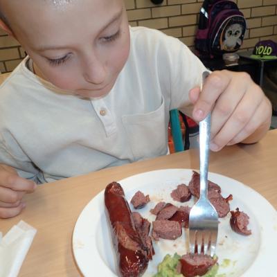 Ein Junge isst im Klassenzimmer eine gegrillte Wurst mit Guacamole