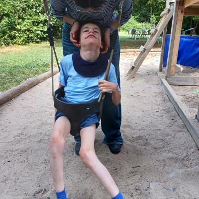 Schüler sitzt in der Schaukel , eine Betreuerin steht hinter ihm und hält den Kopf , er ist noch misstrauisch , wie er es findet 