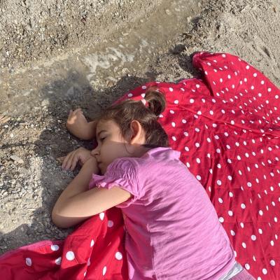 Ein Mädchen liegt auf der Picknickdecke vor dem Bachlauf und streckt ihre Hand in das Wasser