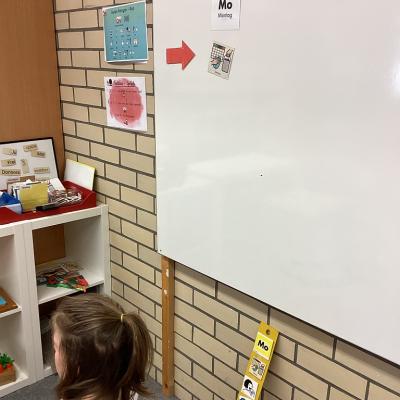 Eine Person sitzt vor einer Tafel und hält eine Bilddkarte in der Hand. Auf der Tafel hängen die Bildkarten 