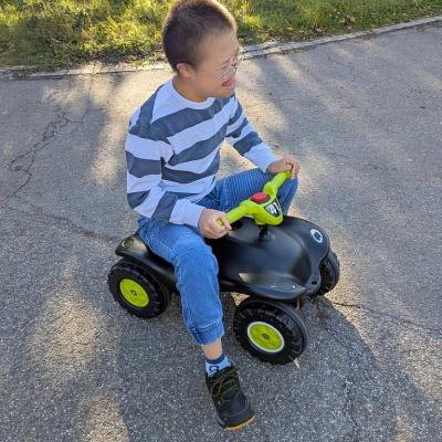 Eine Junge sitzt auf einem schwarze Bobbycar. Er lacht und streckt die Zunge aus seinem Mund