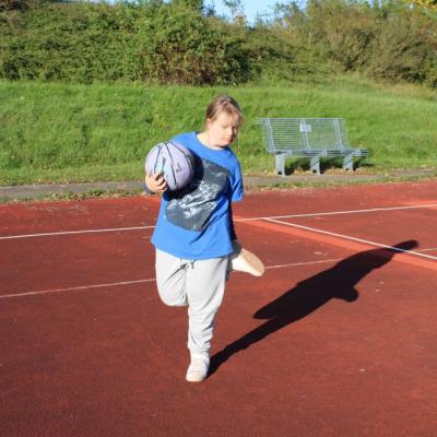 Eine junge Frau steht auf dem Sportplatz auf einem Bein und hält einen Basketball in der Hand
