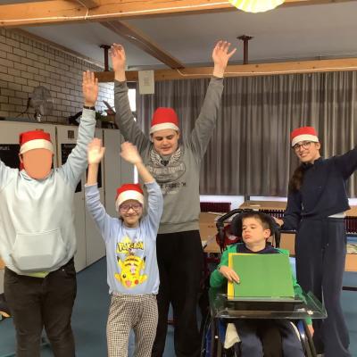 Auf dem Foto sind 3 Schüler und 2 Schülerinnen in Weihnachtsmützen zu sehen. Sie heben die Arme nach oben. Ein Schüler zeigt ein grünes Schild. 