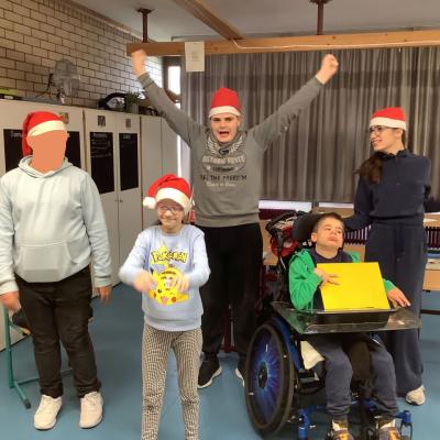 Auf dem Foto sind 3 Schüler und 2 Schülerinnen in Weihnachtsmützen zu sehen. Sie lassen die Arme kreisen. Ein Schüler zeigt ein gelbes Schild. 