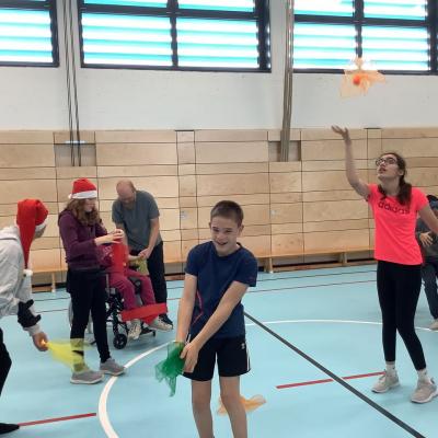 Auf dem Foto sind 2 Schülerinnen und 3 Schüler in Weihnachtsmützen zu sehen. Sie werfen Tücher in die Luft und fangen sie wieder auf. 