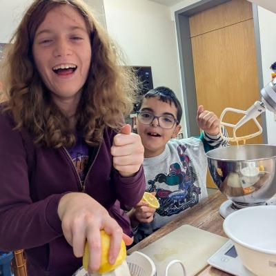 Ein Junge und ein Mädchen stehen in der Küche und raspeln eine Zitrone und kneten Teig, lachen in die Kamera