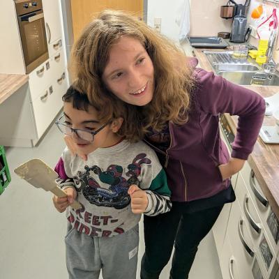 Ein Junge und ein Mädchen stehen in der Küche und lachen lustig in die Kamera