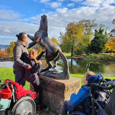 Schülerin steht vor einer Figur aus Bronze, die Figur ist ein steigendes Pferd auf einen Steinblock, die Schülerin streichelt die Figuren von der Seite