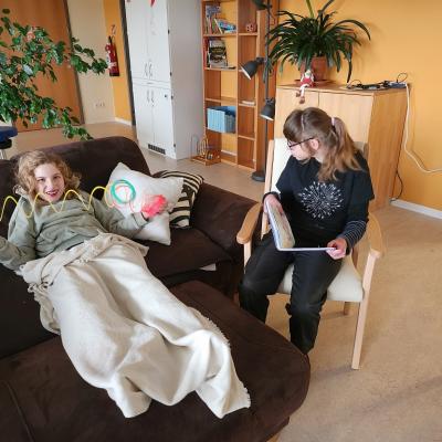 Eine Schürerin liegt auf dem braunen Sofa ist zu gedeckt mit einer weisen decke, sie spielt mit einer Spirale