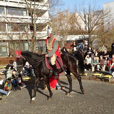 Sankt Martin mit Schwert und halbem Mantel mittig, im Hintergrund viele Zuschauer