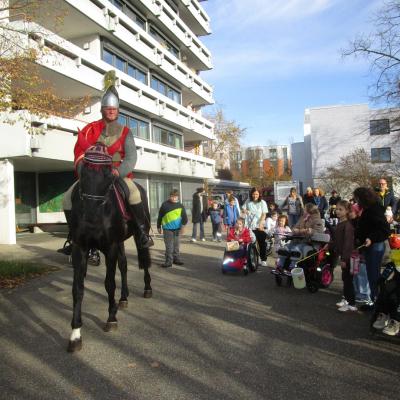 Vor dem mehrstöckigen Internatsgebäude: Sankt Martin zieht voraus, Kinder, Jugendliche und Erwachsene hinterher