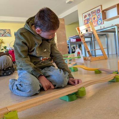 Ein Junge sitzt auf dem Boden bei der Kugelbahn und freut sich darüber