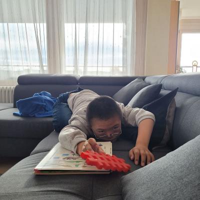 Ein Junge liegt auf dem Sofa auf den Bauch und hält ein Spielzeug in die Kamera. 