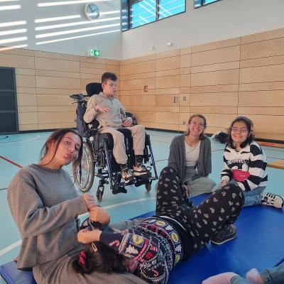 Eine Gruppe von Kindern und Erwachsenen sitzen in der Turnhalle und unterhalten sich 