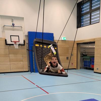 Ein Junge schaukeln hoch hinaus auf der Netzschaukel und lacht in die Kamera