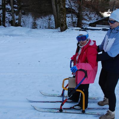 Ghofran läuft am Skilator in der Loipe und lächelt in die Kamera. Frau Fecke stützt sie von hinten.