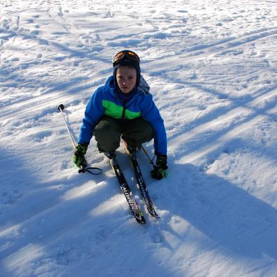 Luca hockt mit Ski quer über die Loipe und schaut etwas erschöpft in die Kamera.