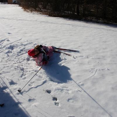 Sophia liegt mit Ski an den Beinen im Schnee und grinst in die Kamera.