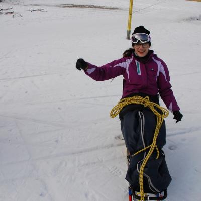 Marija sitzt im Langlaufschlitten. Auf ihrem Schoß liegt ein gelbes Seil. Sie hat die Arme in der Bewegung erhoben.