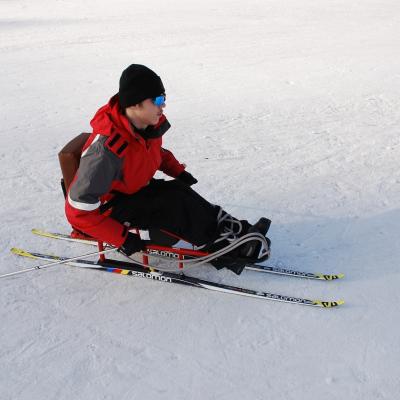 Maik fährt im Langlaufschlitten von links nach rechts über den Schnee.
