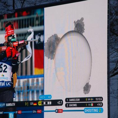 Auf einem großen Bildschirm sieht man Philipp Nawrath beim Stehen-Schießen. Daneben in groß eine weiße Zielscheibe.