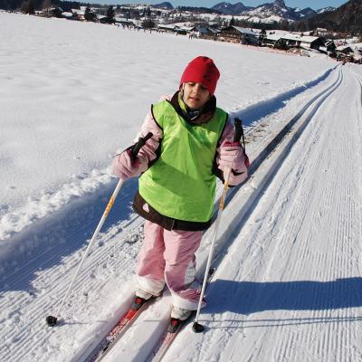 Sophia läuft in der Loipe. Im Hintergrund sieht man Häuser und bewaldete Berge.