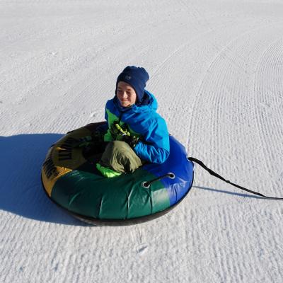Luca hockt in einem Reifen auf dem Schnee. Er kneift die Augen vor der Sonne zu und grinst.
