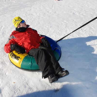 Maik liegt in einem Reifen auf dem Schnee und wird von Herrn Kling, den man nur abgeschnitten sieht gezogen.