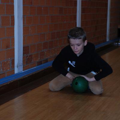 Luca kniet auf der Kegelbahn und rollt eine Kugel frontal nach vorne.