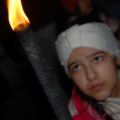 Im Fokus ist eine brennende schwarze Fackel. In der Unschärfe dahinter sieht man Ghofran, die die Flamme anschaut.