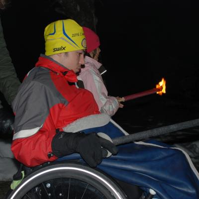 Maik hält eine brennende Fackel und wird von Frau Fecke nach rechts geschoben. Neben ihm geht Sophia. Auch sie hält eine brennende Fackel.