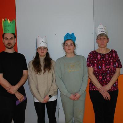 Herr Kling, Lena, Frau Fecke und Frau Gauch stehen vor einer Wand und schauen ernst in die Kamera. Sie tragen alle Kronen aus Papier mit ihren Namen.