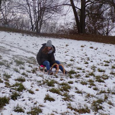 Eine Jugendliche fährt mit einem Holzschlitten eine  Hügel hinab. Sie ist warm eingepackt und lacht. 