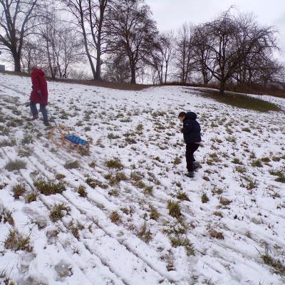 Eine Frau und ein Junge laufen den Hügel wieder hoch. Die Frau zieht einen Holzschlitten 