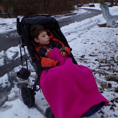Eine Junge sitzt in einem Buggy. Er ist warm angezogen und mit einer Decke zugedeckt. 