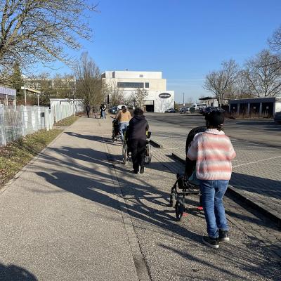 Mehrere Menschen gehen gemeinsam einen Gehweg entlang, einige schieben Rollstühle.