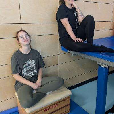 zwei Frauen sitzen beim Trampolin und lachen in dei Kamera