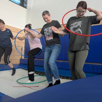 4 Frauen stehen auf dem Trampolin und führen einen reifen duch Arme und Kopf