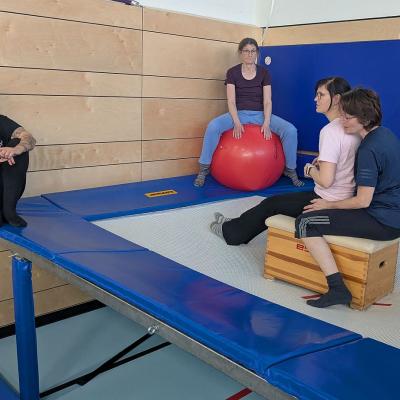 zwei Frauen sitzen auf einem Kasten auf dem Trampolin, zwei Frauen sitzen am Rand