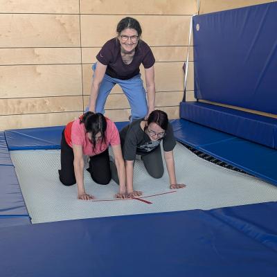 zwei Frauen knien auf dem Trampilin eine oben drauf, wie eine kleinen Pyramide