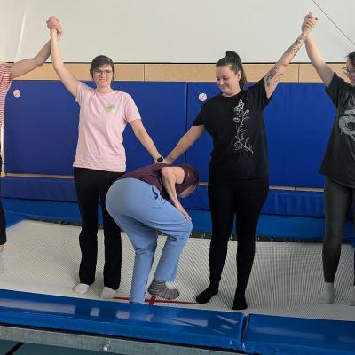 4 Frauen bilden eine Reihe auf dem Trampolin, 1 andere Frau schlängelt sich durch