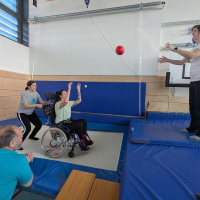 Eine Rollstuhlfahrerin und eine Frau springen auf dem Sprungtuch und eine andere Person wirft den Ball zum spielen zu 