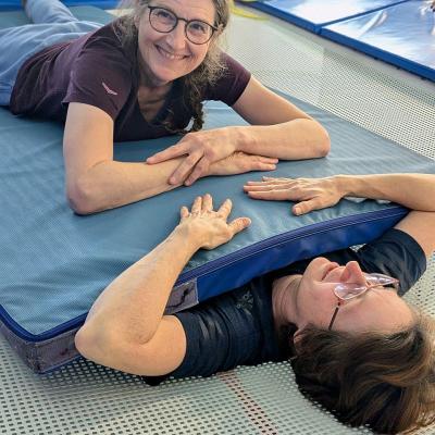 Zwei Frauen liegen auf dem Trampolin übereinander, zwischen ihnen liegt eine Turnmatte