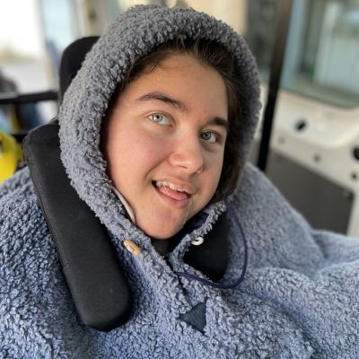 Eine junge Frau im Rollstuhl lacht in die Kamera