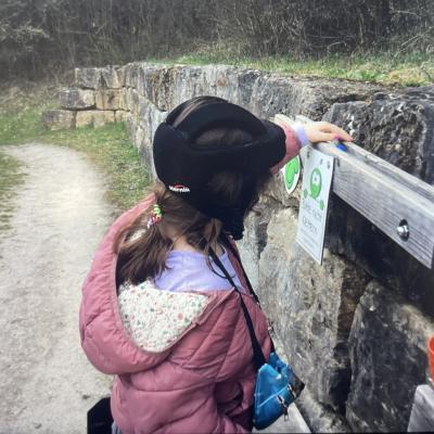 Ein Mädchen legt eine Kugel in eine Kugelbahn. Die Kugelbahn ist draußen an einer Mauer ang