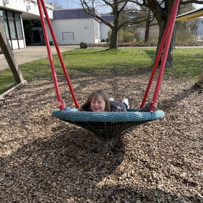 Eine junge Frau liegt in einer Nestschaukel. Sie lacht in die Kamera
