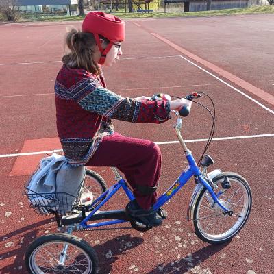 Schülerin sitzt auf ihrem blauen Fahrrad , sie hat einen roten Helm auf und fährt auf dem roten Sportplatz
