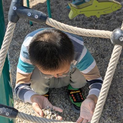 ein Junge spielt auf dem Spielpatz mit Kies